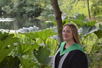 Zarah in academic dress beside large plants