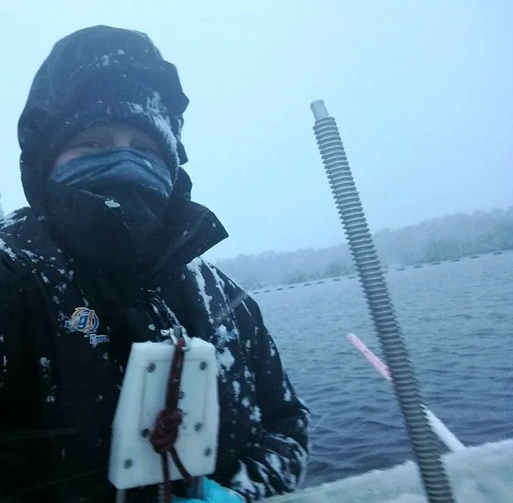 A bundled-up field researcher holding measuring equipment in snow